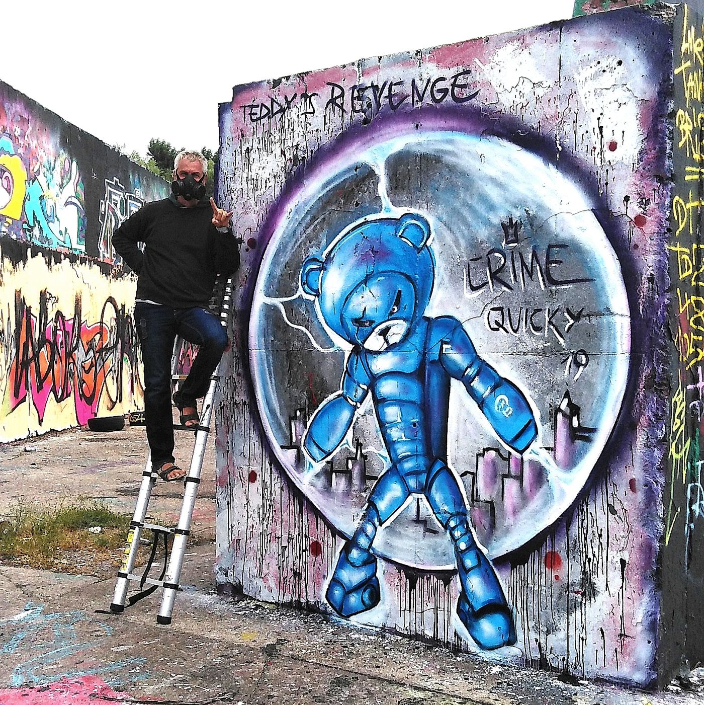 Graffiti mit blauer Comic-Figur auf einer Schallschutzwand, daneben eine Leiter