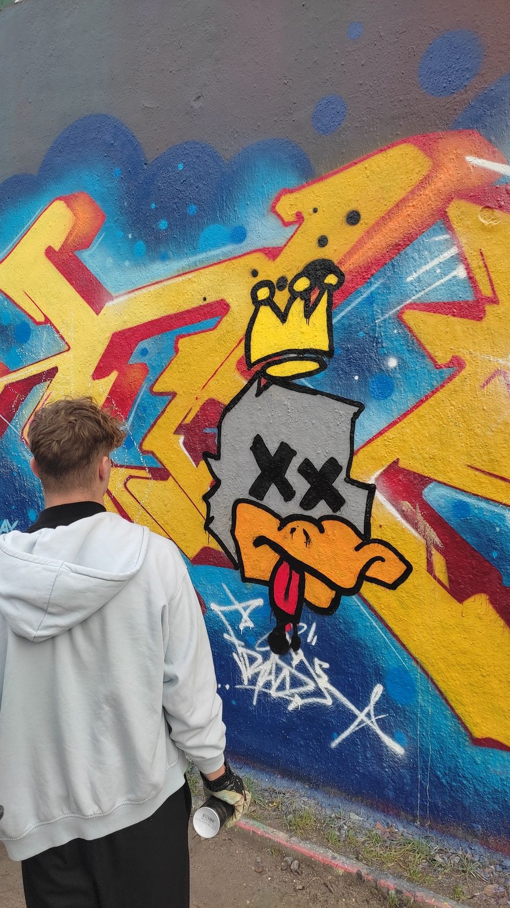 Zwei Personen vor einem farbigen Graffiti an einer Mauer während einer Unterrichtseinheit